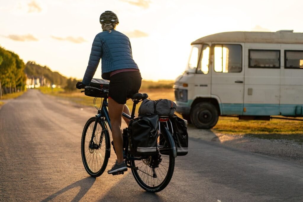 femme sur un vélo portant de sacs de voyages avec en arrière plan une caravane garé
