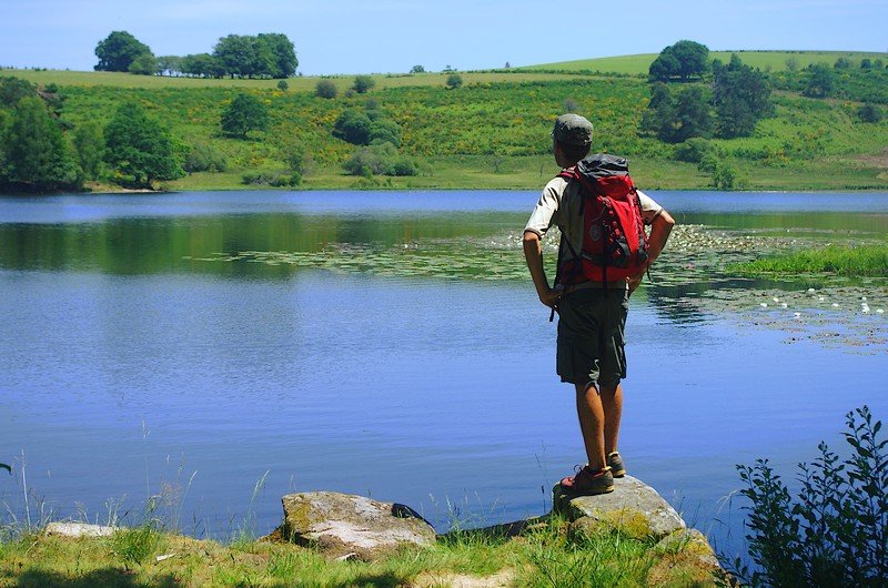 Monsieur devant un lac portant un sac à dos de randonnée 